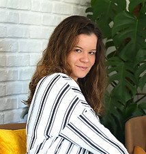 Zdjęcie przedstawia młodą kobietę w kasztanowych włosach za ramiona, która się uśmiecha.