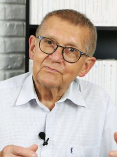 Starszy pan w okularach korekcyjnych z siwymi włosami z przypiętym mikrofonem do białej koszuli