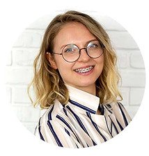 Zdjęcie przedstawia młodą kobietę w okrągłych cienkich oprawkach. Ma blond włosy, które sięgają do ramion. Kobieta się uśmiecha z widocznym aparatem na zębach. 